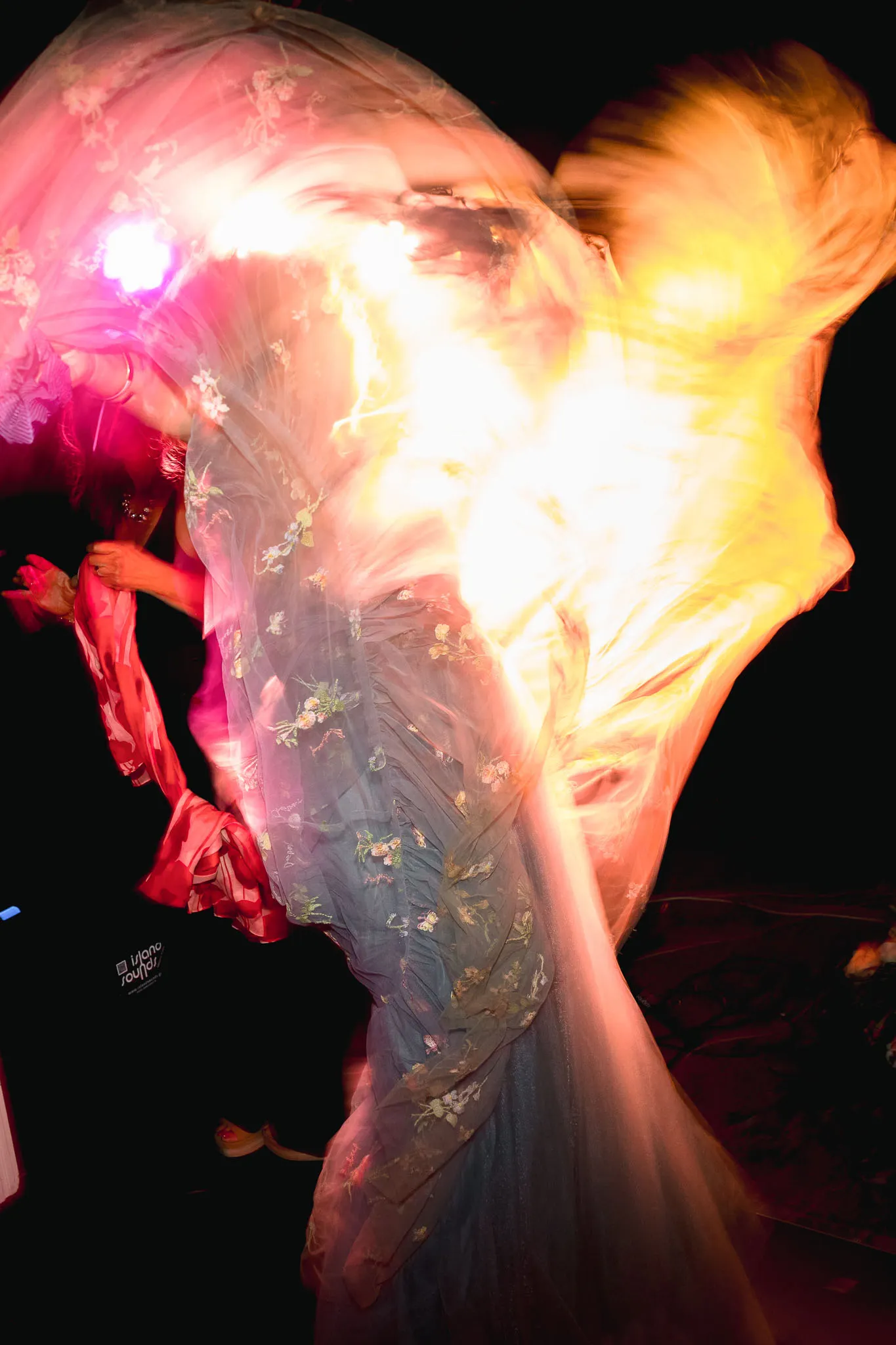 A dynamic scene with a person dancing in a flowing, floral-patterned dress, surrounded by swirling lights and vibrant motion, evoking energetic elegance.
